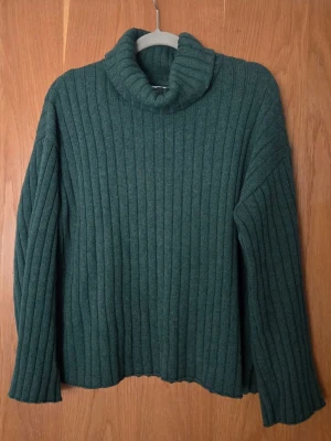 Grön ribbad polotröja Stockh LM Studio - Mysig mörkgrön polotröja från Stockh LM Studio i storlek M. Tröjan är ribbstickad med hög polokrage och långa ärmar. Perfekt för kyliga dagar och enkel att styla till olika outfits.