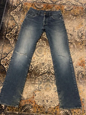 Blå vintage jeans från Gul & Blå  - Säljer ett par klassiska blå jeans från Gul & Blå med rak/baggy passform. Jeansen har slitningar vid knät för en riktigt vintage vibe. Femficksmodell med läderpatch bak och snygga detaljer. Tillverkade i bomull och har en autentisk tvättad look. Smått slitna vid hälarna.