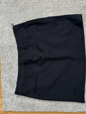 Svart kortkjol från H&M - Svart kort kjol från H&M i storlek 36. Kjolen har en rak passform, diskreta ”låtsas” fickor fram och stängs med dragkedja i sidan. Tillverkad i ett mjukt bomullsmaterial som känns bekvämt och stilrent. Aldrig använd. 