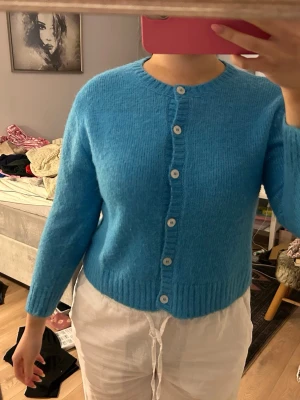 Blå stickad kofta med knappar - Mysig blå stickad kofta med rund halsringning och vita knappar hela vägen framtill. Koftan har lång ärm och ribbade muddar vid ärmslut och nederkant. Perfekt att slänga på sig när det är lite kyligt ute. OBSERVERA‼️‼️‼️ det står storlek L på koftan men den sitter som en xs-S