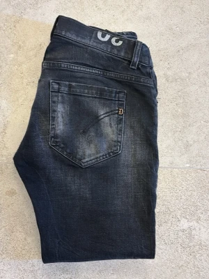 Svarta jeans från dondup med slitningar - Säljer ett par svarta jeans från Dondup med slitningar på benen och tvättad look. Bälteshällor och en liten D-detalj på bakfickan. Materialet är klassisk jeans. 