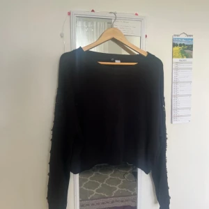 Svart stickad tröja med spetsdetaljer - Svart stickad tröja från H&M med långa ärmar och snygga spetsdetaljer i blommönster längs ärmarna. Tröjan har en lite croppad passform och rund halsringning. Perfekt för dig som vill ha något stilrent med en twist.