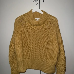 Gul stickad polotröja från H&M - Mysig gul stickad polotröja från H&M i storlek L. Tröjan har en chunky ribbstickad design, hög polokrage och långa ärmar. Materialet är en blandning av polyester, akryl och ull vilket gör den både varm och skön. Perfekt för kyliga dagar.