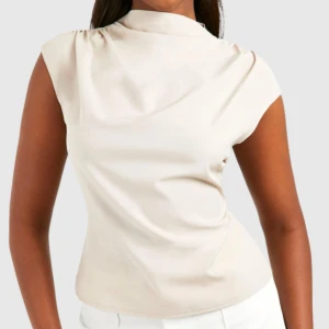 Beige blus  - Säljer en stilren beige blus från Boohoo med omlott-detalj vid axeln och diskret dragkedja i ryggen. Aldrig använd!! Säljer för att den är för liten💕💕