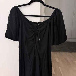 Svart klänning  - Svart klänning från Lager 157 med snygg snörning framtill och breda, puffiga kortärmar. Klänningen har en offshoulder-design och är helt ny med prislapp kvar