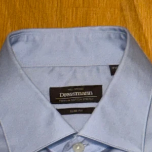 Ljusblå skjorta Dressmann slim fit - Snygg ljusblå skjorta från Dressmann i slim fit-modell. Skjortan har klassisk krage, långa ärmar och vita knappar framtill. Tillverkad i mjuk bomull med stretch för extra komfort. Perfekt för dig som gillar stilrena och enkla plagg. Använd en gång, var för stor så säljer den. 