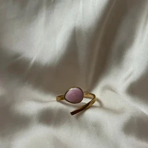Guldfärgad ring med rosa sten - Unik guldfärgad ring med öppen design och en droppformad, ljusrosa sten. Ringen har en modern och minimalistisk look som sticker ut med sin mjuka form och glansiga finish. Perfekt för dig som gillar stilrena accessoarer med en touch av färg. Justerbar öppning 💞Stainless Steel 💗 18 k guldpläterad 😍