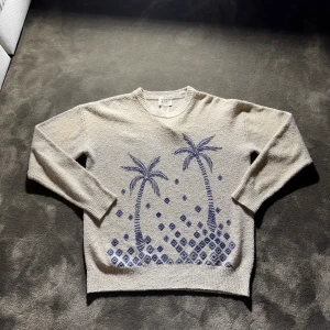Unik stickad tröja Scotch & Soda - Stickad beige tröja från Scotch & Soda med mörkblå broderat palmträdsmotiv och geometriska mönster på framsidan. Rund hals och långa ärmar, perfekt för dig som gillar chill vibes och snygga detaljer. Materialet är mjukt och känns riktigt skönt mot huden. Tröjan är i nyskick!