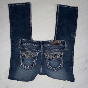 Lågmidjade bootcut jeans - Säljer ett par blå jeans som liknar Miss Me med snygga detaljerade bakfickor med bling och broderier. Jeansen ska vara bootcut/straight och jag skulle mer säga straight! De är stretch! De har lite smådefekter som jag kan skicka bild på om så önskas! Storlek M men passar även S