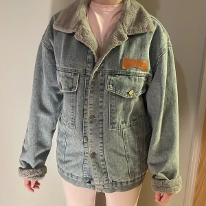 Oversized jeansjacka med teddyfoder - Säljer en ljusblå jeansjacka från Top Denim med mjukt grått teddyfoder och krage. Jackan har två stora bröstfickor med knappar, knappstängning framtill och en cool oversized passform. Perfekt för dig som gillar streetstyle och vill ha det extra mysigt.