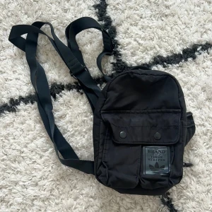 Svart ryggsäck från Adidas <3 - Svart Adidas mini ryggsäck med justerbar axelrem och flera fack. Väskan har en logotyp framtill och text på baksidan. Använt skick och har några defekter, har mer att ge <3