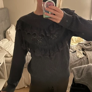 Grå stickad volangtröja  - Mysig grå stickad tröja från Lindex med lång ärm och snygga volangdetaljer i spets över bröstet. Tröjan har ett hålmönster och ribbade muddar vid hals, ärmslut och nederkant. Perfekt för dig som gillar en söt och trendig look.💞💞stl 164 men skulle säga att den är som en xs/s