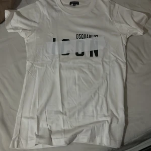 Vit ICON t-shirt från Dsquared2 - Snygg vit t-shirt från Dsquared2 i storlek S med trycket 'ICON' i svart på bröstet. Klassisk rund hals och korta ärmar. Tillverkad i mjuk bomull som känns skön mot huden. Perfekt för dig som gillar stilrena och trendiga plagg med statement-tryck.