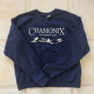 Mörkblå sweatshirt Chamonix H&M Divided - Mörkblå sweatshirt från H&M Divided i storlek S med vit broderad text 'CHAMONIX THE FRENCH ALPS' och skidmotiv på bröstet. Tröjan har rund hals, ribbade muddar och lång ärm. 