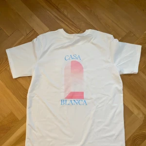 Vit Casa Blanca t-shirt med tryck - Vit t-shirt från Casa Blanca med korta ärmar och ett stort grafiskt tryck i rosa och blått på . SAMMA DAG DU KÖPER SAMMA DAG JAG FRAKTAR