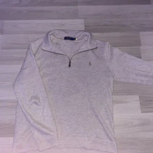 Beige half zip tröja från Polo Ralph Lauren - Säljer en stilren beige långärmad tröja från Polo Ralph Lauren med half zip och broderad logga på bröstet. Tröjan har en hög krage och är tillverkad i mjuk bomull, perfekt för lager-på-lager under höst och vinter.