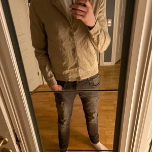 Beige overshirt från Oscar Jacobson - Stilren beige overshirt från Oscar Jacobson med knappar framtill. Passar till finare tillfällen men även dagligt bruk. Säljer pga att jag tycker den är för liten. Finns tecken på användning men inga skador. MVH Pelle