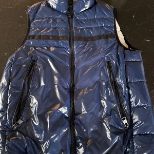 Blå dunväst från Calvin Klein - Fet väst med vattenavvisande matrial. go vit insida. knappt använd! enda nackdel är ett litet hål i ena ficken.