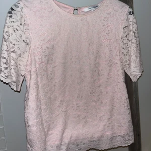 Ljusrosa spetsblus från KappAhl - Säljer en söt ljusrosa blus från KappAhl med korta ärmar och vacker spets över hela toppen. Blusen har rund halsringning och ett feminint, romantiskt uttryck. Perfekt för dig som gillar detaljer och mjuka färger.