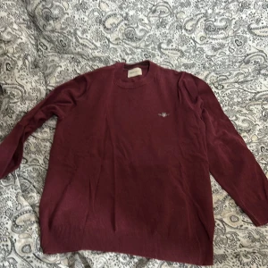 Vinröd stickad tröja från GANT - Vinröd stickad tröja från GANT med rund hals och broderad logga på bröstet. Tröjan har ribbade muddar vid ärmslut och nederkant, samt långärmad passform. Perfekt för dig som gillar klassisk och stilren design. Den är i väldigt bra skick men tyvär för liten för mig, är lite mindre storlek S, pris ör självklart inte hugget i sten än🤩