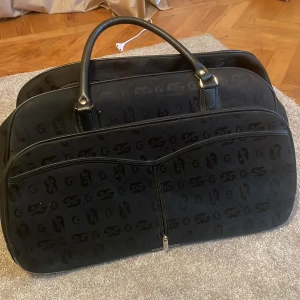 Supersnygg weekendväska💕 - Stor svart resväska från med monogram över hela väskan. Väskan har två rejäla handtag, dragkedja framtill och förstärkt botten med skyddande fötter. Tillverkad i syntetmaterial med detaljer i skinnimitation. Perfekt för dig som vill resa med stil. Kan finnas små defekter men inget som stör funktionen😊💕 Lämna bud skambud undanbedes