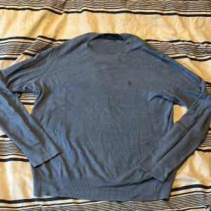 Blå Ralph lauren tröja - Säljer en blå stickad tröja från Polo Ralph Lauren med rund halsringning och diskret broderad logga på bröstet. Klassisk och stilren modell, köpte tröjan från en kompis som säljer kläder, man kan se små trådar som börjar lossna på baksidan av tröjan (går att se på sista bilden) men tror inte att det är ett sånt stort problem. Säljer pga att jag aldrig använder och färgen var inte riktigt min typ. Den passar storleken 14-16 jag är 163cm lång och den är lite stor på mig.