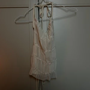 Beige omlott linnetopp från SHEIN - Supersöt beige linnetopp från SHEIN i storlek S. Toppen har snörning i ryggen och tunna axelband som knyts i nacken. Dekorerad med volangdetaljer och spetsband 🌟