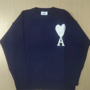 Mörkblå stickad tröja från Ami Paris - Säljer en mörkblå stickad tröja från Ami Paris med ett stort vitt hjärta och bokstaven A på bröstet. Tröjan har rund halsringning och långa ärmar, perfekt för dig som gillar stilrena detaljer med en twist.