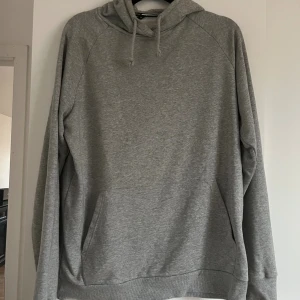 Grå hoodie från SOC med huva - Enkel och stilren grå hoodie från SOC i storlek M. Tröjan har huva med snörning, känguruficka framtill och långa ärmar. 