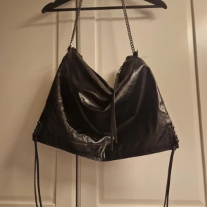 Superfin Zara väska!!💕💕 - Cool svart axelväska i mjukt skinn med silverfärgad kedja som axelrem. Väskan har en slouchy form, dragkedja upptill och långa snören på sidorna för extra edge. Perfekt storlek för allt du behöver och har en innerficka med dragkedja.