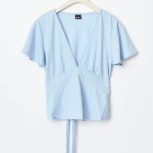 Ljusblå omlottopp från Gina Tricot - Supersöt ljusblå omlottopp från Gina Tricot med v-ringning och korta, lite fladdriga ärmar. Toppen har knytband i midjan som ger en snygg siluett och är gjord i mjuk bomull. Perfekt att styla med jeans.