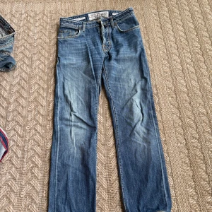 Jacob Cohen blå jeans slim fit - Snygga blå jeans från Jacob Cohen med klassisk slim fit och kontrastsömmar. Handgjorda i Veneto, Italien. Jeansen har fem fickor, patch med logga i blått på baksidan och coola slitningar framtill. Perfekt för dig som gillar exklusiva denim och stilren look.
