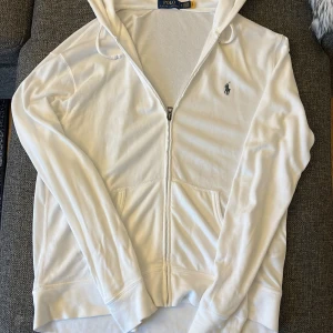 Vit hoodie från Polo Ralph Lauren - Vit hoodie från Polo Ralph Lauren med dragkedja framtill och klassisk logga broderad på bröstet. Tröjan har huva med snörning, två fickor. En skön sommar tröja! Använt ungefär 3-4 gånger