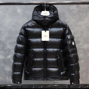 Svart Moncler pufferjacka med huva Stolek 2=M - Säljer en svart pufferjacka från Moncler med glansig finish och huva. Jackan har dragkedja framtill, två sidofickor med dragkedja och en liten ficka på ärmen med Moncler-logga. Perfekt för kalla dagar och har en riktigt snygg streetstil.