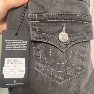 True Religion Joey Low Rise Flare Jeans - Snygga gråa jeans från True Religion i modellen Joey Low Rise Flare. De har låg midja, utsvängda ben och coola fickor med lock och silverfärgade knappar bak. Jeansen är i stretchigt denim och har en faded look som ger extra edge. Jätte fina men har ej använt eftersom storleken ej passar. (Min vän har boxorna på bilden) Pris kan diskuteras.  
