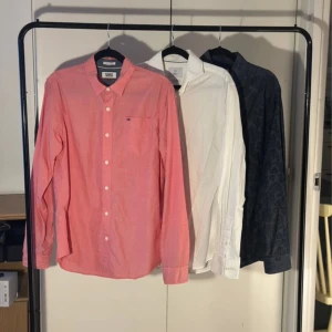 3 skjortor  - Tre skjortor säljes: en ljusrosa skjorta från Tommy Jeans med klassisk krage och bröstficka, en vit skjorta från Bläck med skräddad passform och en mörkblå skjorta med subtilt mönster. Alla har långa ärmar och knappar framtill. Perfekt för dig som gillar stilrena och snygga skjortor.