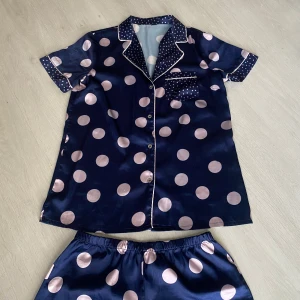 Mörkblå prickiga pyjamasshorts i satin - Snygga mörkblå pyjamasshorts i glansigt satinmaterial med stora ljusbeiga prickar. Shortsen har elastisk midja och kontrasterande småprickiga detaljer vid benslut. Perfekta för en chill kväll hemma.