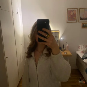 Vit ribbad kofta med dragkedja från BikBok - Säljer en vit ribbstickad kofta från BikBok i storlek XS. Tröjan har en bred krage, hel dragkedja framtill och långa ärmar. Materialet är stickat och ger en mysig känsla, perfekt för lager-på-lager. Enkel och clean look som funkar till jeans eller kjol.