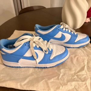 Nike Dunk Low blå och vita sneakers - Nike Dunk Low sneakers i fräsch blå och vit färg. Skorna  är i jätte bra skick och har använts fåtal gånger. De är unika skor som är bekväma och snygga! Pris går att diskutera, 38/39.
