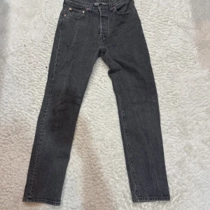 Levi's 501 mörk grå jeans W28 L30 - Svarta Levi's 501 jeans med klassisk rak passform och femficksdesign. Jeansen har knappgylf, snygga bakfickor med Levi's signatur och är tillverkade i slitstarkt denim. Perfekta för dig som gillar en tidlös och clean look.