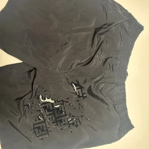 Svarta badbyxor från Fendi - Svarta badbyxor från Fendi med elastisk midja och snörning. Fendi-loggan kommer fram när  byxorna blir blöta som ger en cool touch. Shortsen är tillverkade i ett lätt och bekvämt material, perfekta för bad dagar!