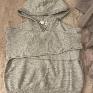 Grå stickad hoodie med huva - Mysig grå stickad hoodie från Gina med huva och snörning. Tröjan har långärmade ribbade muddar och en relaxed passform som är perfekt för chill dagar. Enkel och stilren design som funkar till jeans eller mjukisbyxor. Storlek 170 men passar mig som bär S.