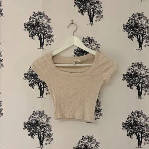 Beige croppad topp från H&M Divided - Säljer en beige croppad topp från H&M Divided. Toppen har korta ärmar, rundad halsringning och är ribbad i materialet. Perfekt för dig som gillar enkel och stilren design med en slim passform. Superenkel att matcha med dina favoritjeans eller kjol.