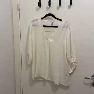Vit v-ringad blus från JDY - Säljer en stilren vit blus från JDY i storlek 38. Blusen har v-ringning, trekvartsärmar med knappdetalj och en lätt strukturerad yta. Perfekt för dig som gillar en enkel men snygg look.