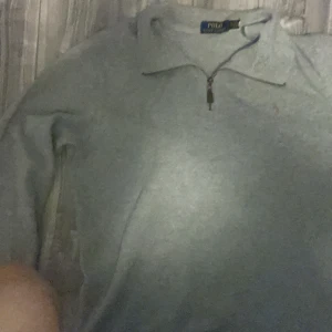 Grå half zip tröja från Polo Ralph Lauren - Snygg grå långärmad tröja från Polo Ralph Lauren med half zip och klassisk broderad logga på bröstet. Tröjan har en mjuk känsla och passar perfekt för chill dagar. Stilren design med krage och diskret dragkedja framtill.