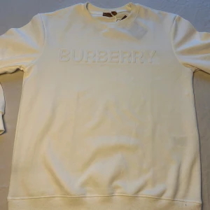 Vit sweatshirt Burberry,  - Vit sweatshirt  Burberry med upphöjt BURBERRY-tryck på bröstet. Tröjan har rund hals, ribbade muddar och är tillverkad i mjuk bomull. Perfekt för dig som gillar stilrena och klassiska plagg med exklusiv känsla.