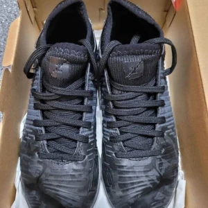 Puma Future Z 4.1 IT Jr fotbollsskor - Svarta Puma Future Z 4.1 IT Jr fotbollsskor med asfaltgrå detaljer och grafiskt mönster på sidorna. Skorna har snörning, platt sula och rund tå. Materialet är syntet med stickad ovandel för extra komfort. Perfekt för inomhusfotboll och träning.