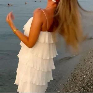 Vit omlottklänning med volanger - Supersöt vit kortklänning med tunna axelband och flera lager volanger som ger en riktigt flowig look. Perfekt till studenten. Skriv om fler frågor🩷