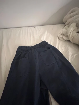 Mörkblå wide mjukisbyxor med snörning - Säljer ett par mörkblå mjukisbyxor från 157 i storlek XS. Byxorna har breda ben, medellåg midja med elastisk linning och snörning, samt stora fickor framtill. Perfekta för chill dagar och riktigt skön passform.