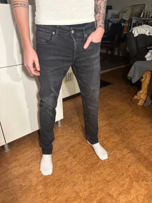 Replay svarta jeans - Snygga Replay Grover eller Annas. jeans i svart tvättad denim med klassisk femficksdesign och smal passform. Byxorna har en normal midja, subtila slitningar och Replay-logga på bakfickan. Perfekt för dig som gillar stilrena och moderna jeans. Modellen är 190 cm lång och väger 70 kg.